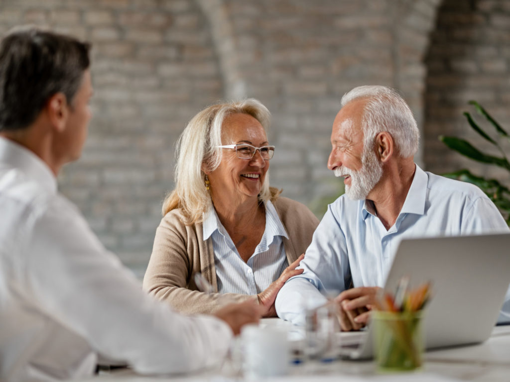 Happy senior couple talking to each other while having meeting with financial advisor.