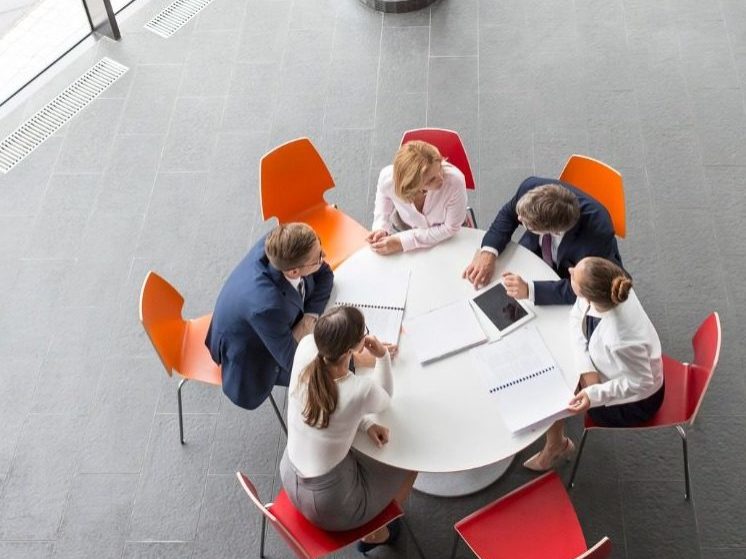 Birds-eye view of Business Individuals sitting at a Round Table with Red and Orange Chairs.